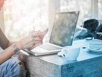 Image of a person in front of a laptop holding a smartphone