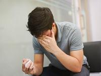 Image of a man holding a tissue in one hand and his head in the other hand