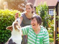 Young carer with woman with learning disabilities playing with dog.