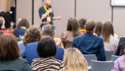 A room full of people sat on chairs listening to a speaker
