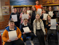 Group of young people in a library holding up drawings
